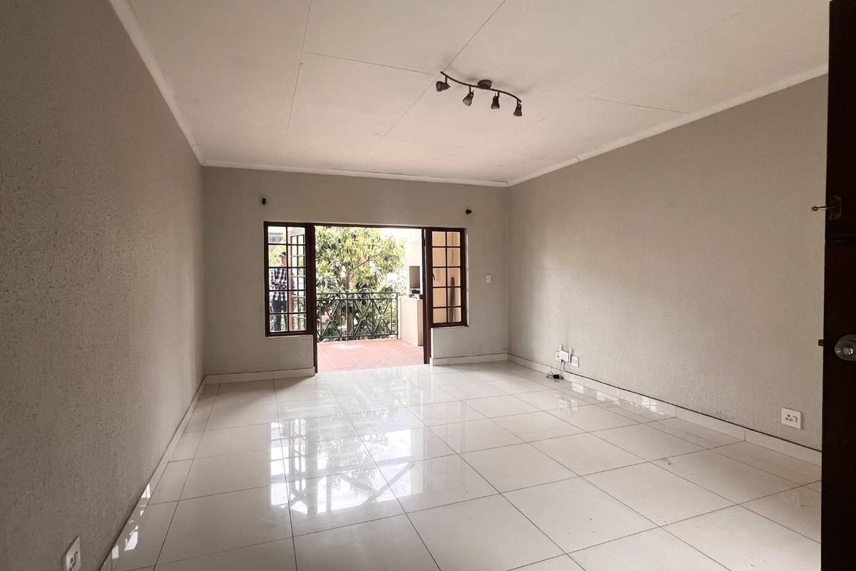 Spacious, empty living room featuring polished white floor tiles, track lighting, and large timber-framed glass doors opening onto a private balcony.