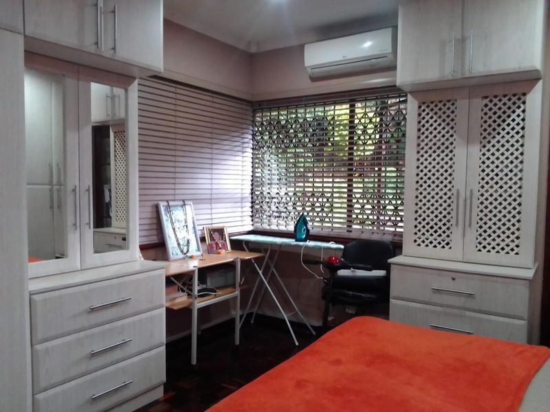 A well-maintained bedroom featuring extensive built-in cabinetry, parquet flooring, and a wall-mounted split-system air conditioner for climate control.