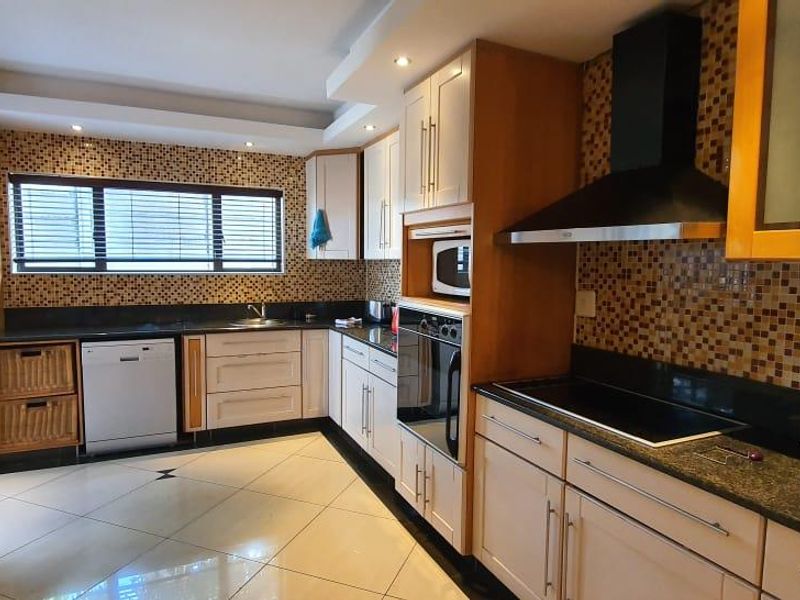 A well-appointed kitchen featuring granite countertops, mosaic tile backsplash, built-in oven, hob, extractor fan, and integrated dishwasher with ample cabinetry.