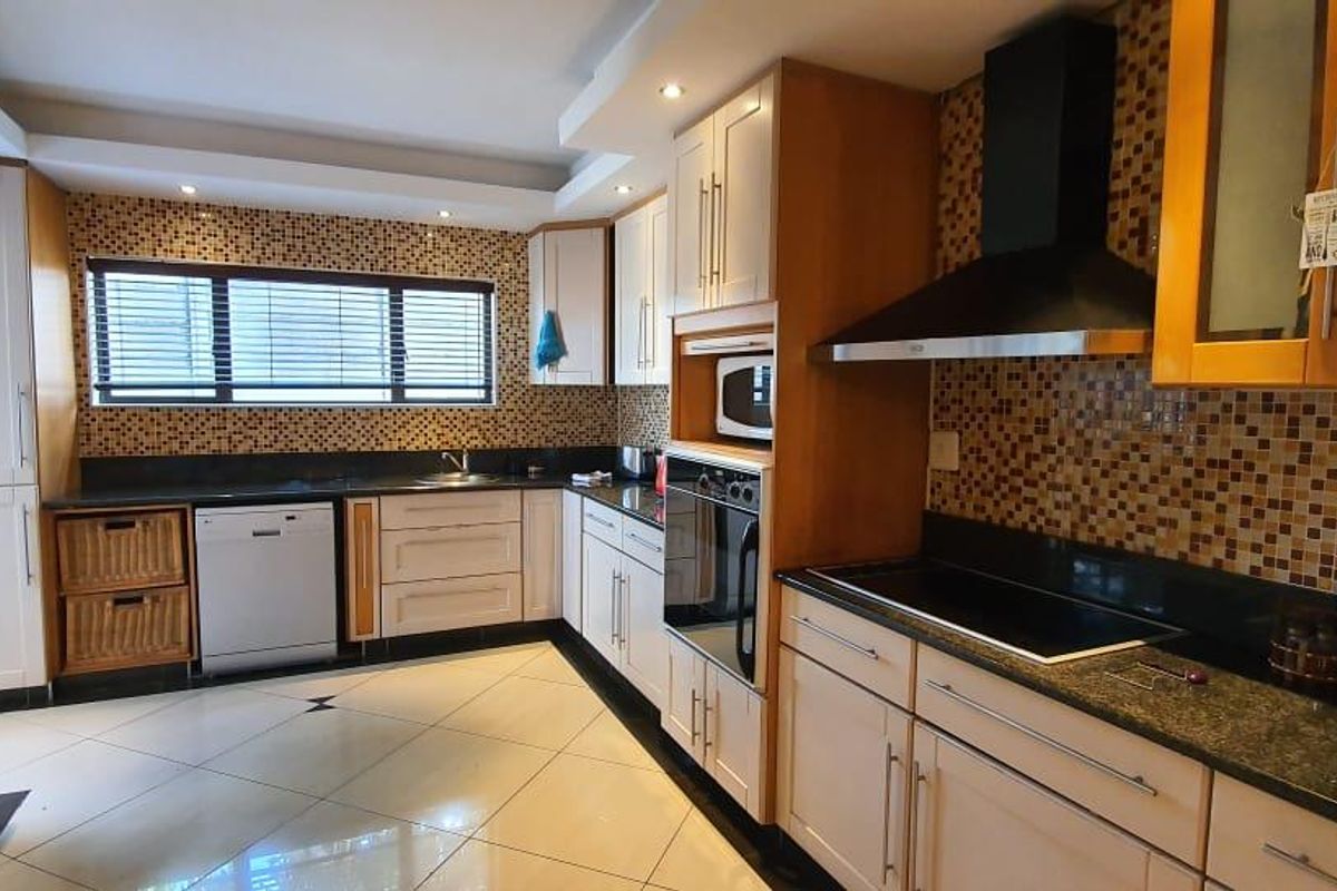 A well-appointed kitchen featuring granite countertops, mosaic tile backsplash, built-in oven, hob, extractor fan, and integrated dishwasher with ample cabinetry.