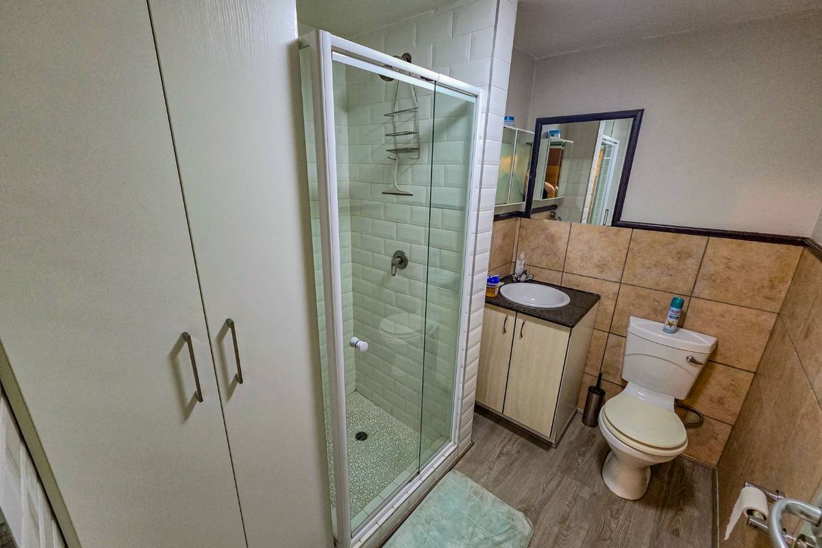 A functional bathroom featuring a glass-enclosed shower, vanity with basin, toilet, and built-in storage cupboard with neutral wall and floor finishes.