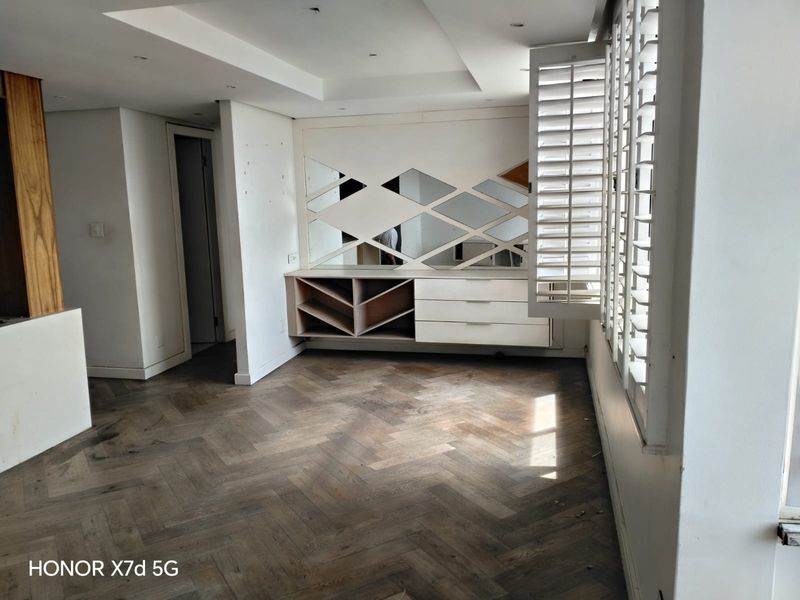 Spacious living area featuring elegant herringbone timber flooring, custom built-in cabinetry with integrated mirrors, and plantation shutters for adjustable natural light.