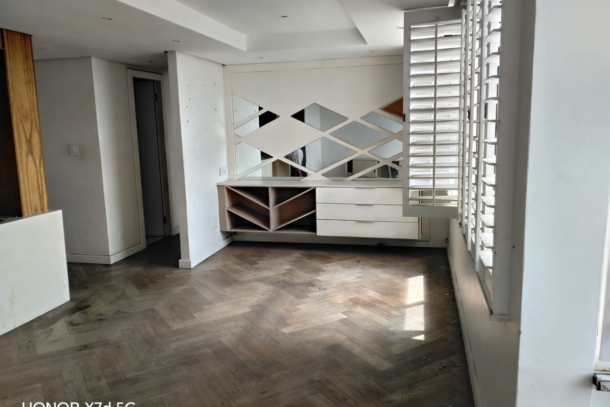 Spacious living area featuring elegant herringbone timber flooring, custom built-in cabinetry with integrated mirrors, and plantation shutters for adjustable natural light.