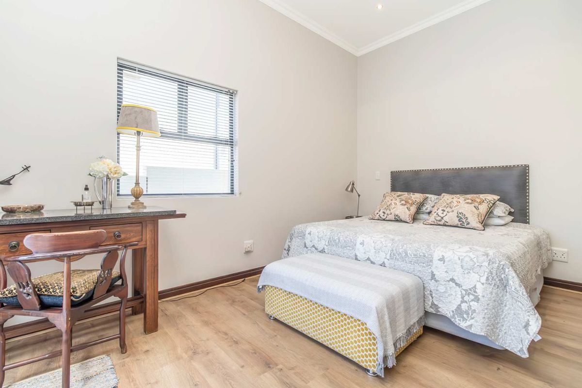 A well-maintained bedroom featuring light wood-look flooring, neutral wall tones, and a window with fitted blinds.