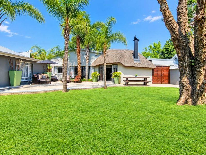 Spacious rear garden featuring a well-maintained lawn, paved patio area, and a distinctive thatched roof structure with an external chimney.