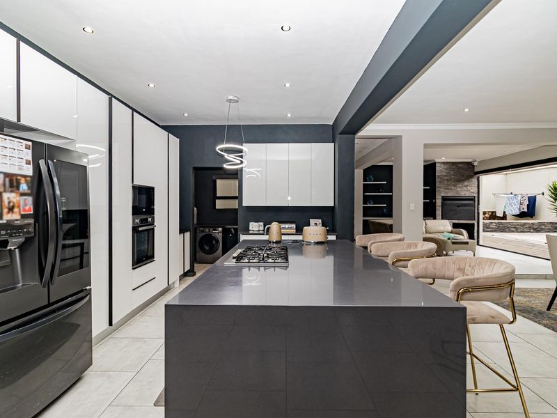 Modern open-plan kitchen featuring a large central island with gas hob, sleek cabinetry, stone countertops, and integrated appliances, flowing into the living area.