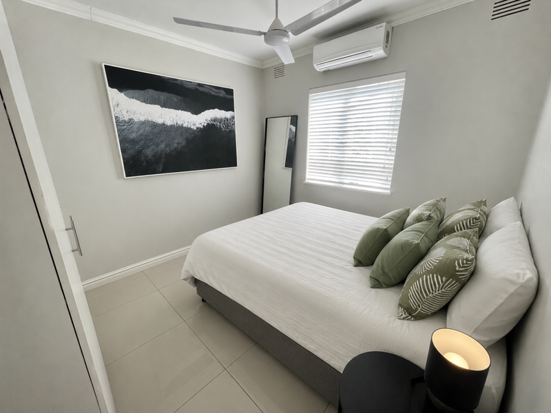 A well-maintained bedroom featuring tiled flooring, a ceiling fan, split-system air conditioning, and a built-in wardrobe with modern finishes.