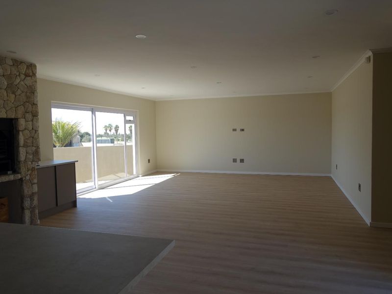 Spacious open-plan living area featuring light laminate flooring, a stone-clad fireplace, and large sliding glass doors leading to an outdoor space.
