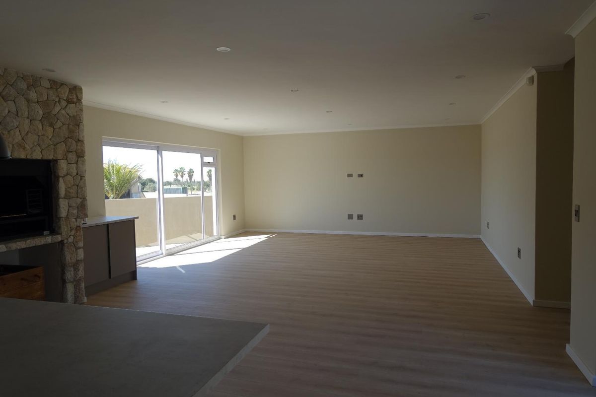 Spacious open-plan living area featuring light laminate flooring, a stone-clad fireplace, and large sliding glass doors leading to an outdoor space.