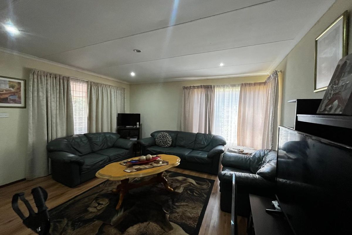 A spacious living room featuring wood-look flooring, recessed ceiling lighting, and large windows with curtains, providing a comfortable and functional living space.