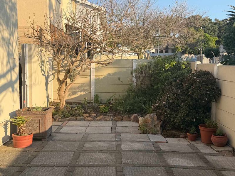 A private rear courtyard featuring a paved patio area, established garden beds, and secure precast concrete boundary walls.