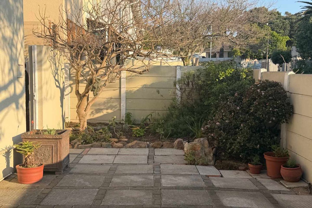 A private rear courtyard featuring a paved patio area, established garden beds, and secure precast concrete boundary walls.