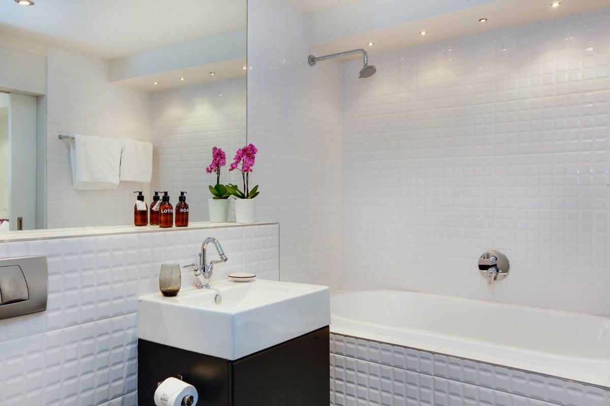 A modern, clean bathroom featuring white tiled walls, a built-in vanity with a basin, and a combined bathtub and shower area.