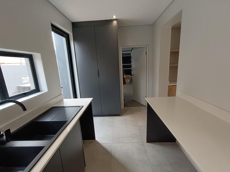 Modern scullery featuring sleek dark cabinetry, stone countertops, an undermount sink with a matte black mixer tap, and neutral floor tiles.
