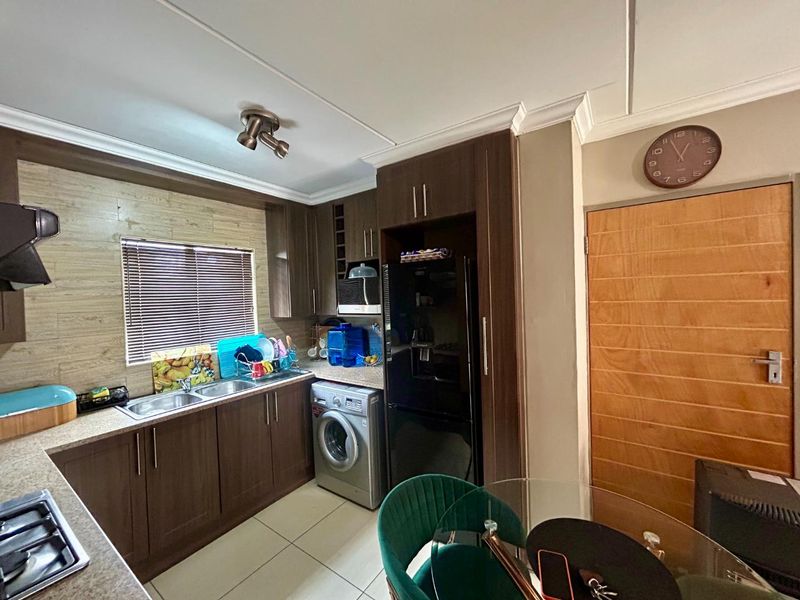 A functional kitchen featuring dark wood cabinetry, laminate countertops, a stainless steel double sink, and tiled flooring with integrated appliance space.
