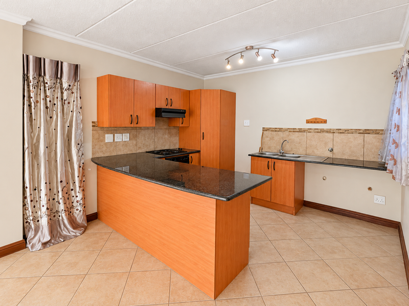 A functional kitchen featuring laminate cabinetry, granite countertops, a built-in hob with extractor fan, and tiled flooring in an open-plan layout.