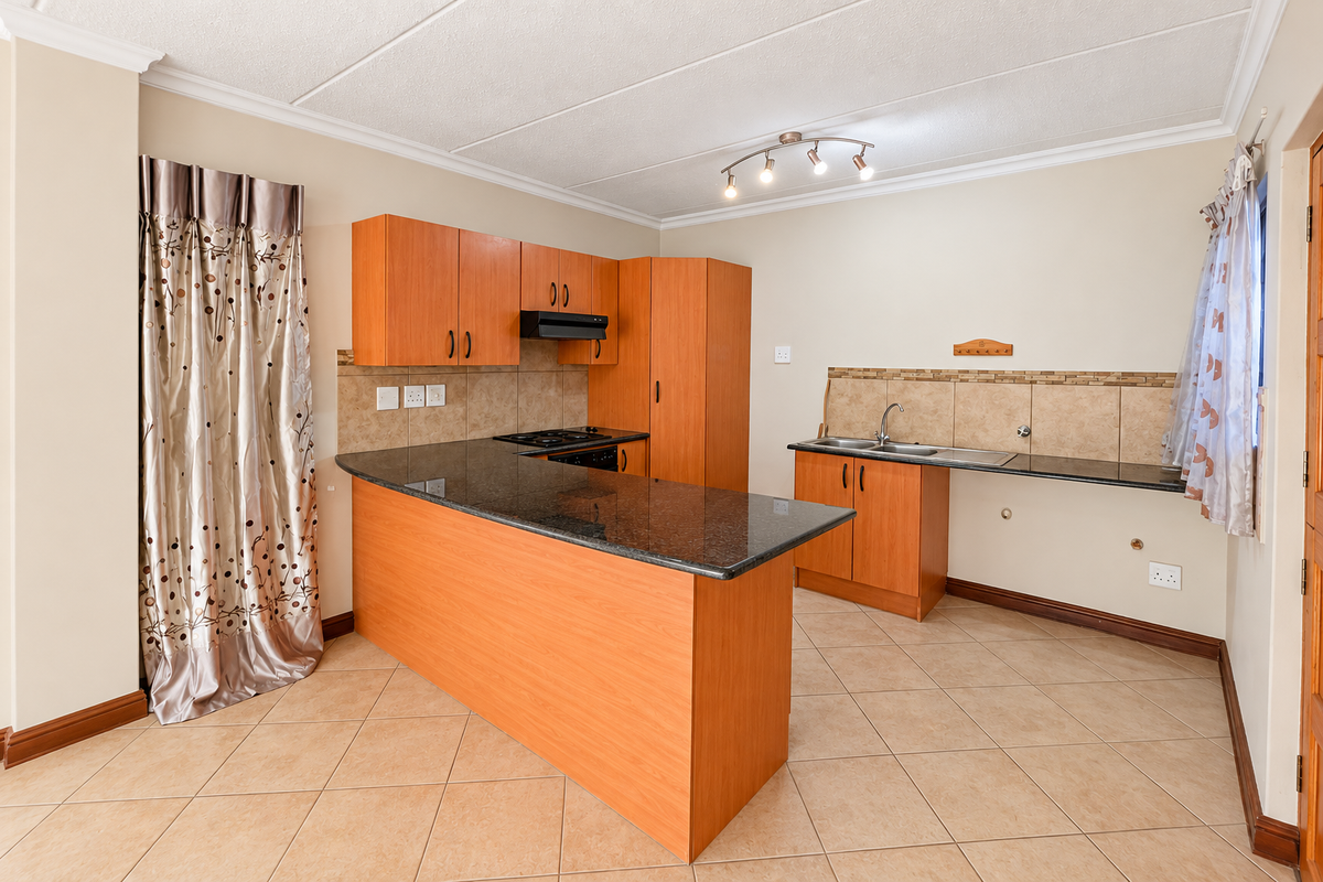 A functional kitchen featuring laminate cabinetry, granite countertops, a built-in hob with extractor fan, and tiled flooring in an open-plan layout.