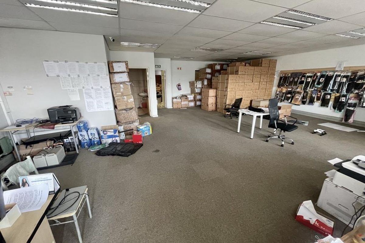 A functional utility or office space featuring a suspended ceiling with recessed lighting and carpeted flooring, currently utilized for storage and workspace.