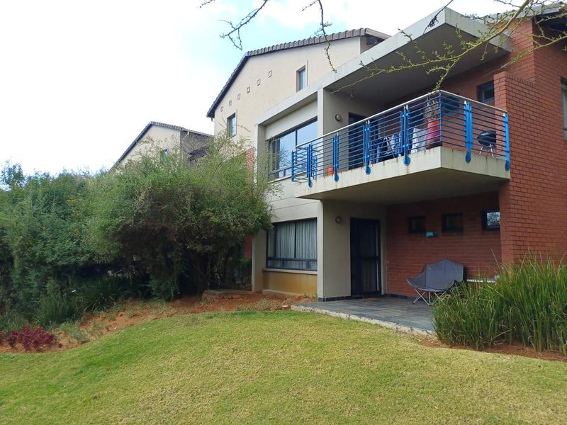 Rear view of a multi-story apartment building featuring a brick facade, a private balcony with metal railings, and a ground-floor paved patio area.