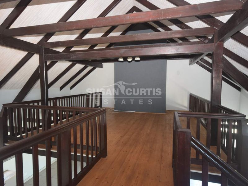 Spacious loft-style living area featuring exposed timber roof trusses, vaulted ceilings, and warm timber flooring with a protective balustrade.