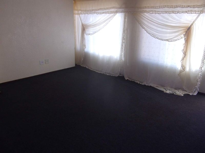 An empty bedroom featuring dark carpeting and natural light from large windows, providing a blank canvas for personalization.