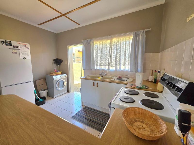 A functional kitchen featuring tiled flooring, built-in cabinetry, a double sink, and an electric stove, with direct access to the exterior.