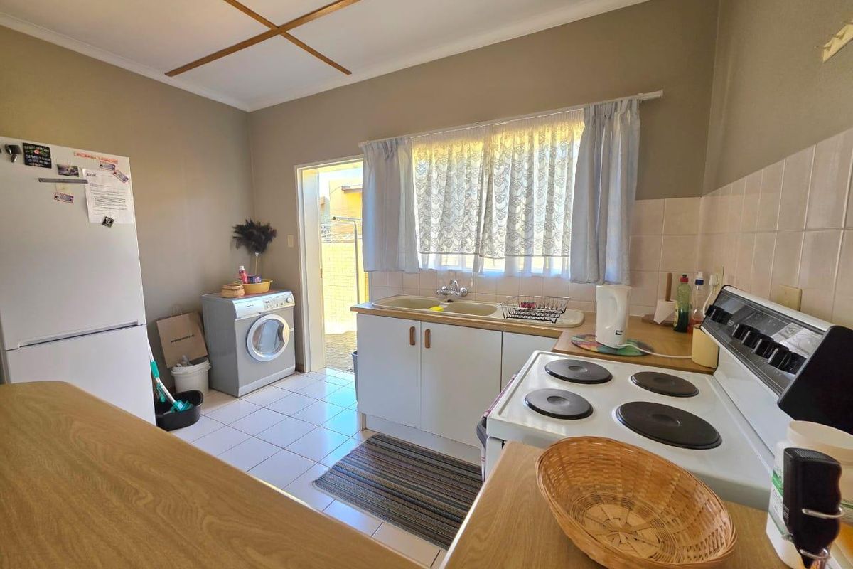 A functional kitchen featuring tiled flooring, built-in cabinetry, a double sink, and an electric stove, with direct access to the exterior.