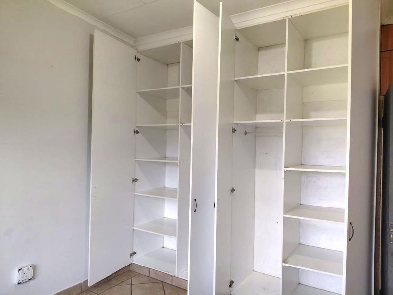 A bedroom interior featuring white built-in cupboards with shelving and hanging space, complemented by tiled flooring.