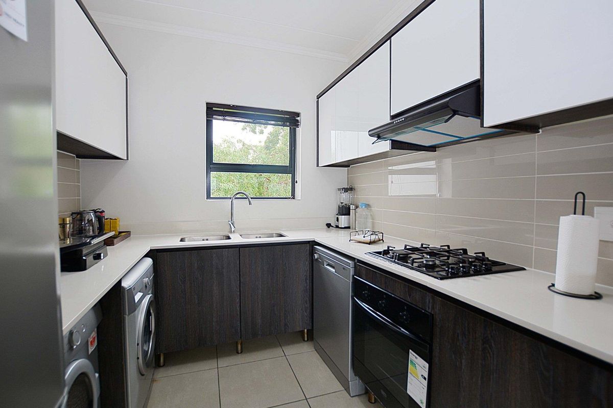 Modern kitchen featuring dark wood cabinetry, stone countertops, gas hob, built-in oven, extractor fan, and integrated space for laundry appliances.