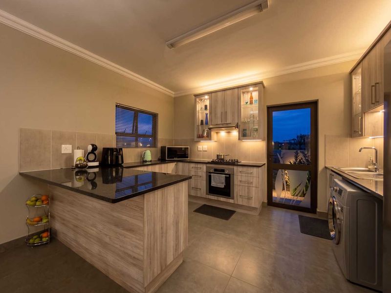 Modern kitchen featuring granite countertops, built-in oven with gas hob, under-cabinet lighting, and ample cabinetry, with direct access to the exterior.