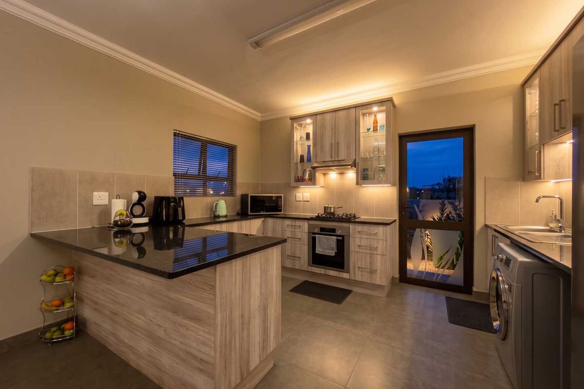 Modern kitchen featuring granite countertops, built-in oven with gas hob, under-cabinet lighting, and ample cabinetry, with direct access to the exterior.