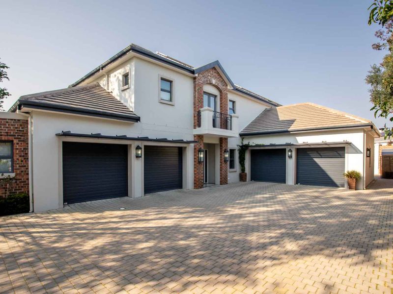 A well-maintained front elevation featuring a triple garage, paved driveway, and a charming balcony with brick detailing.