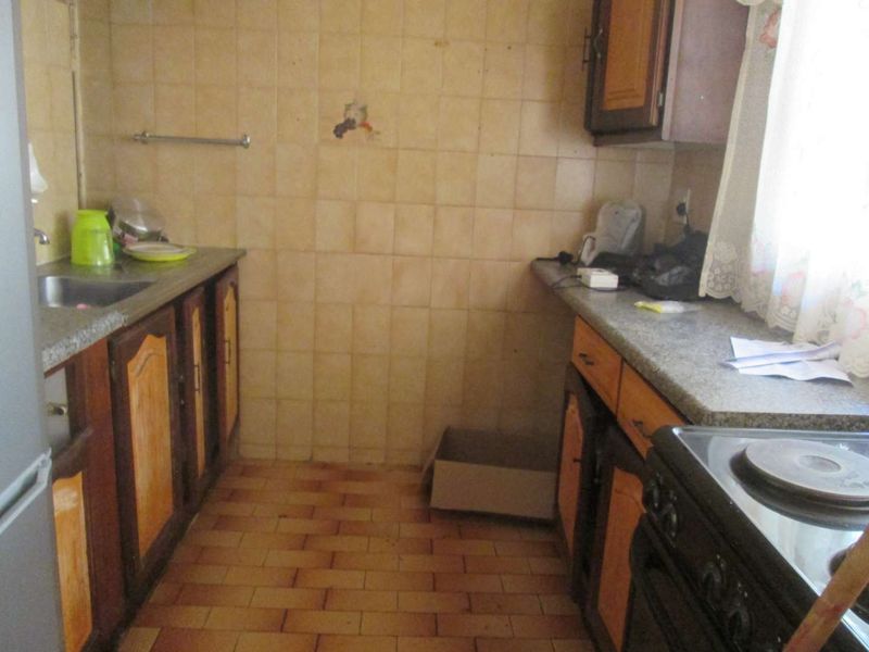 A dated kitchen featuring original cabinetry, tiled backsplash, and laminate countertops, requiring modernization to improve functionality and aesthetic appeal.