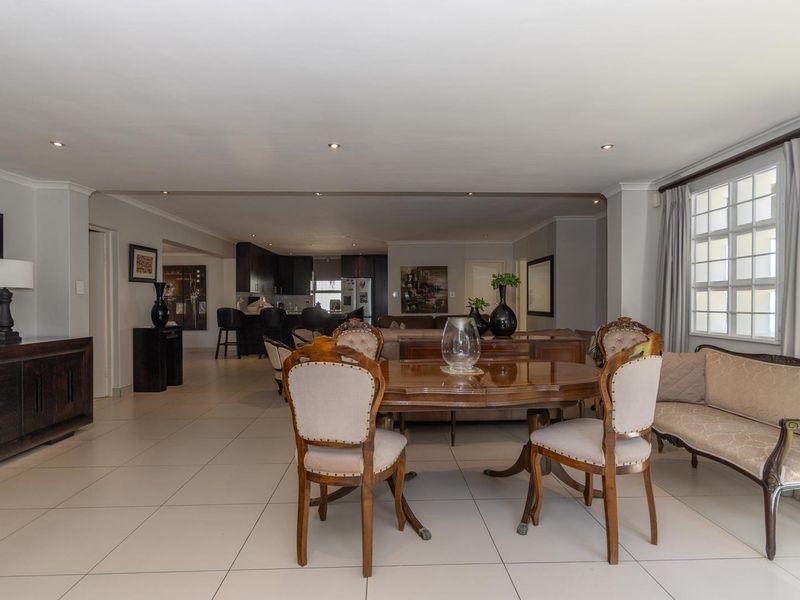Spacious open-plan living and dining area featuring neutral tiled flooring, recessed lighting, and a connected kitchen with dark cabinetry.