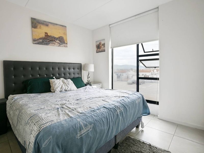 A well-lit bedroom featuring tiled flooring, a built-in wardrobe, and a large window with a roller blind offering exterior views.