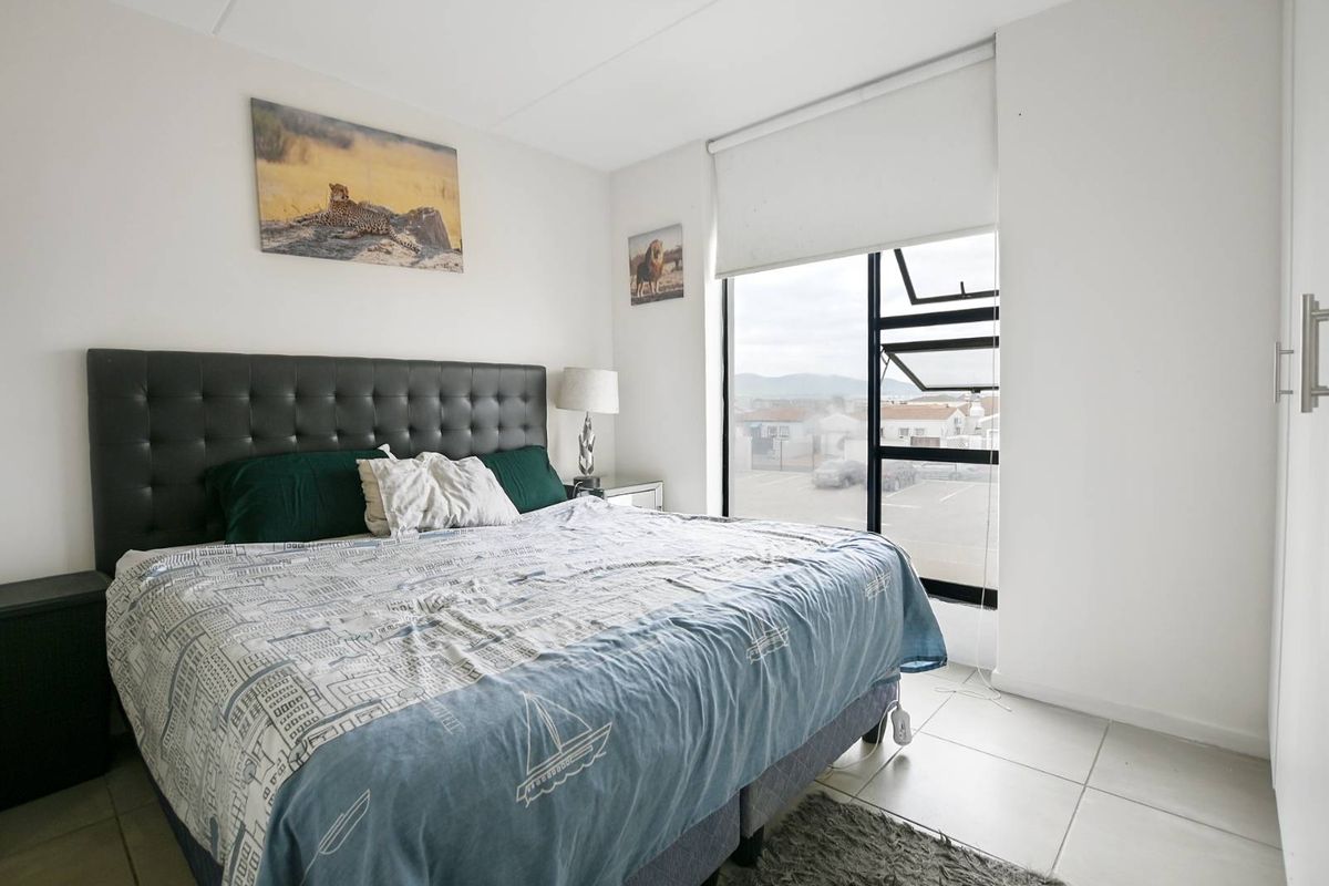 A well-lit bedroom featuring tiled flooring, a built-in wardrobe, and a large window with a roller blind offering exterior views.