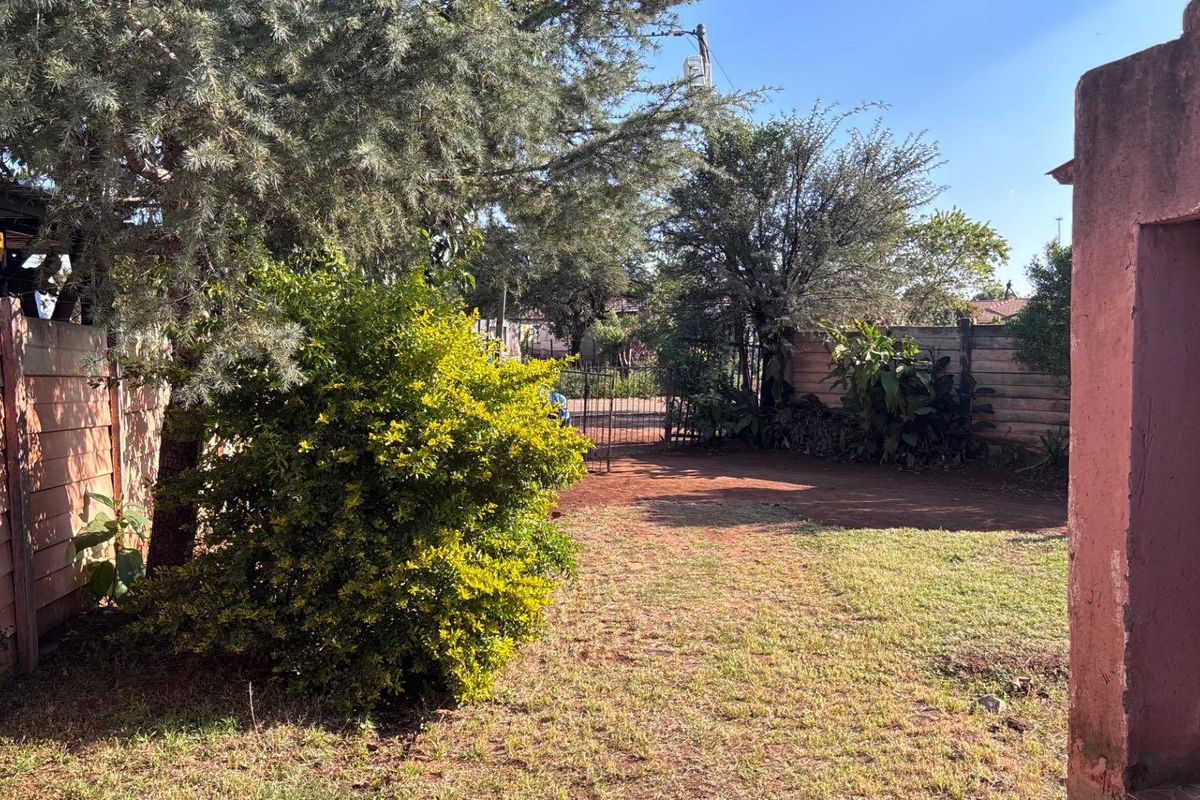 A view of the rear garden area featuring a perimeter boundary wall, mature trees, and an open lawn space.