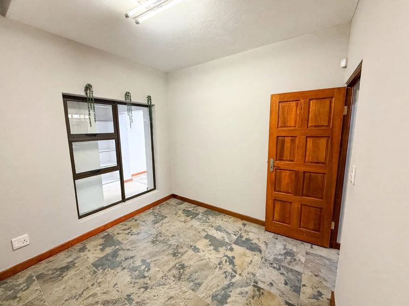 A clean, empty bedroom featuring tiled flooring, a solid timber door, and an aluminium-framed window, providing a neutral space ready for personalization.