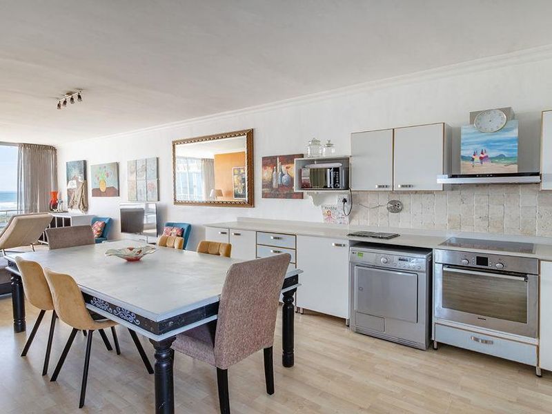Open-plan living and dining area featuring a functional kitchen with built-in appliances and large sliding doors offering expansive ocean views.