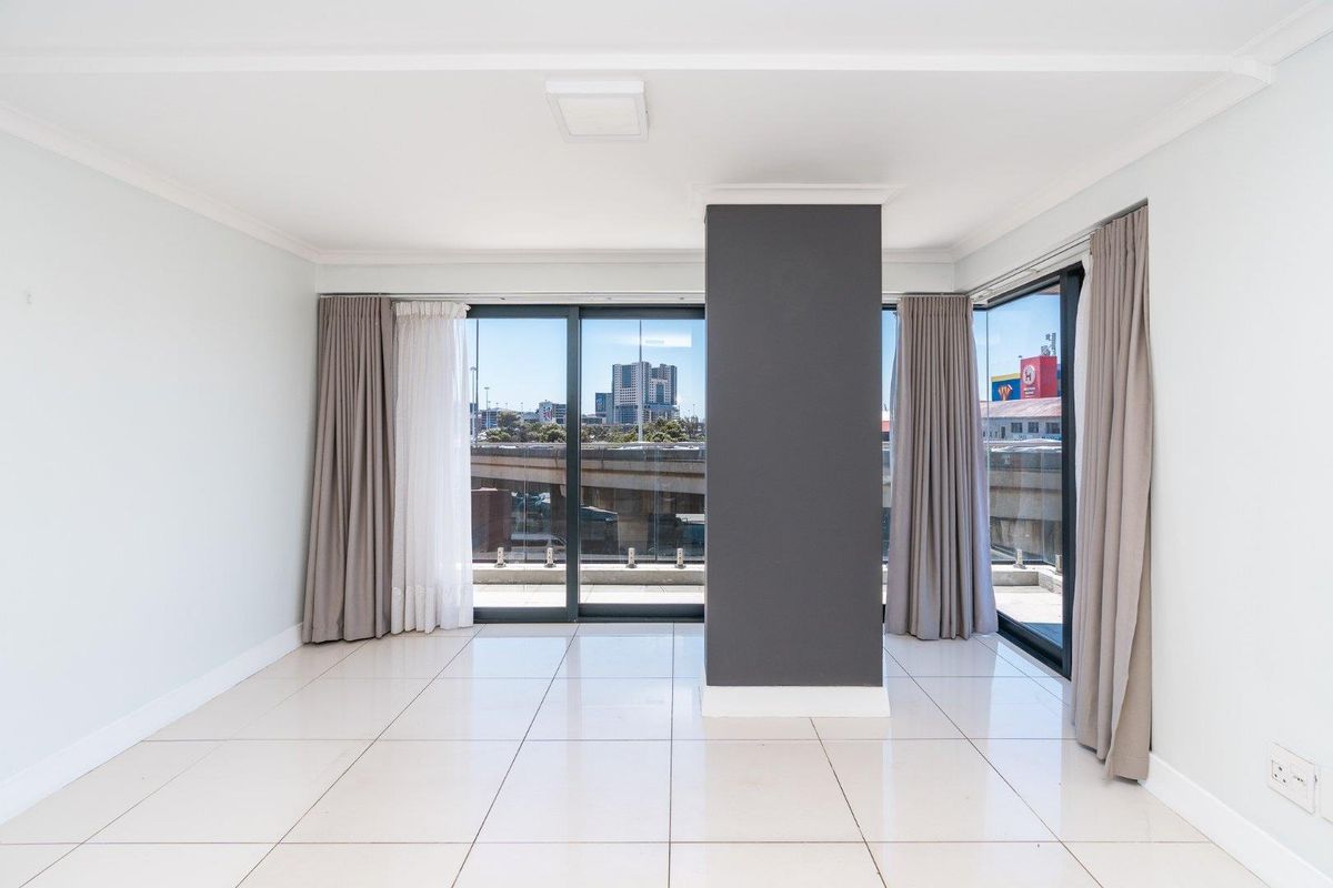 Bright and spacious living area featuring large sliding glass doors, neutral tiled flooring, and a modern central pillar with views of the surrounding cityscape.