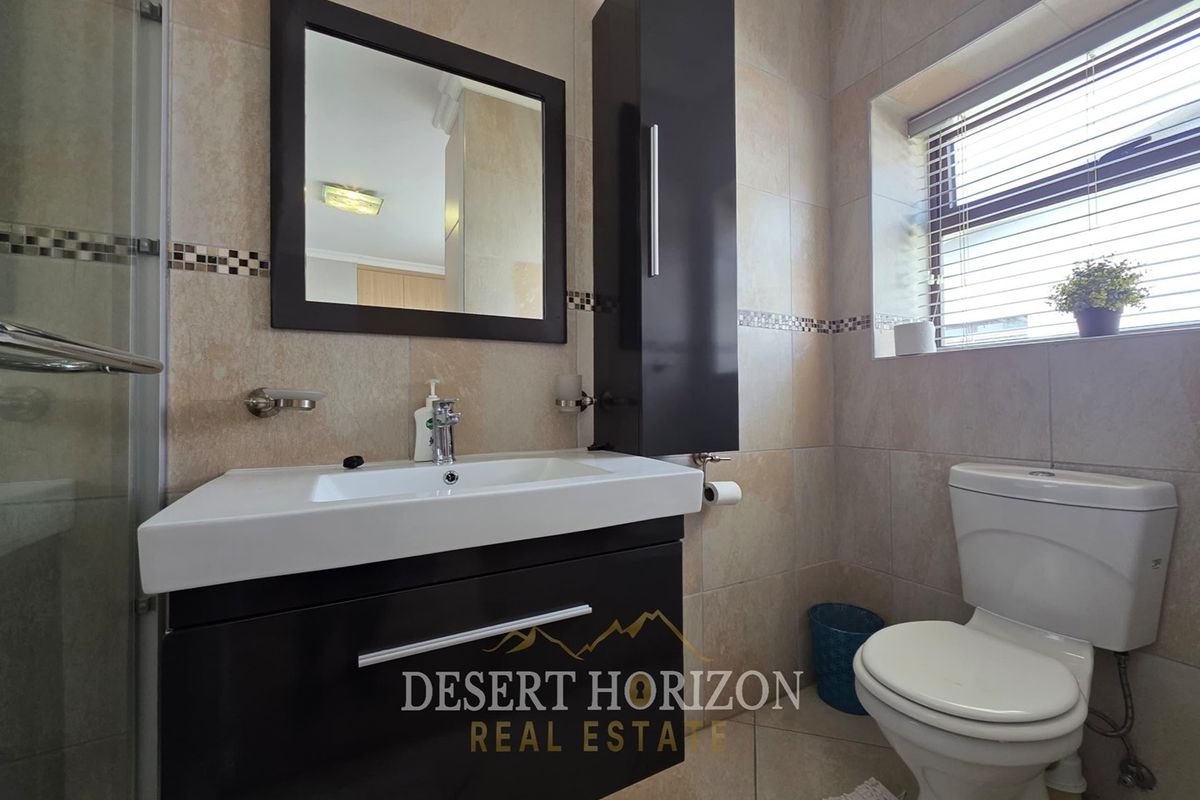Modern bathroom featuring a vanity cabinet with basin, wall-mounted storage, toilet, and a glass-enclosed shower with neutral wall and floor tiling.