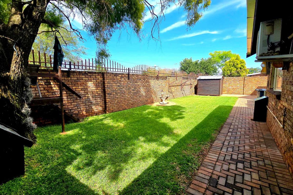 A well-maintained rear garden featuring a brick boundary wall with security spikes, a paved walkway, and a small storage shed.