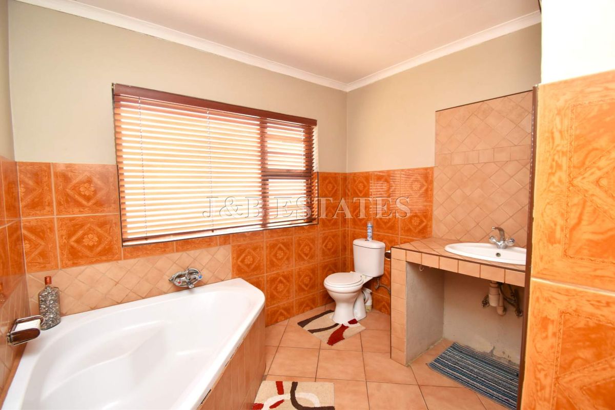 A functional bathroom featuring a corner bathtub, a toilet, and a built-in vanity with a basin, finished with traditional ceramic wall and floor tiles.