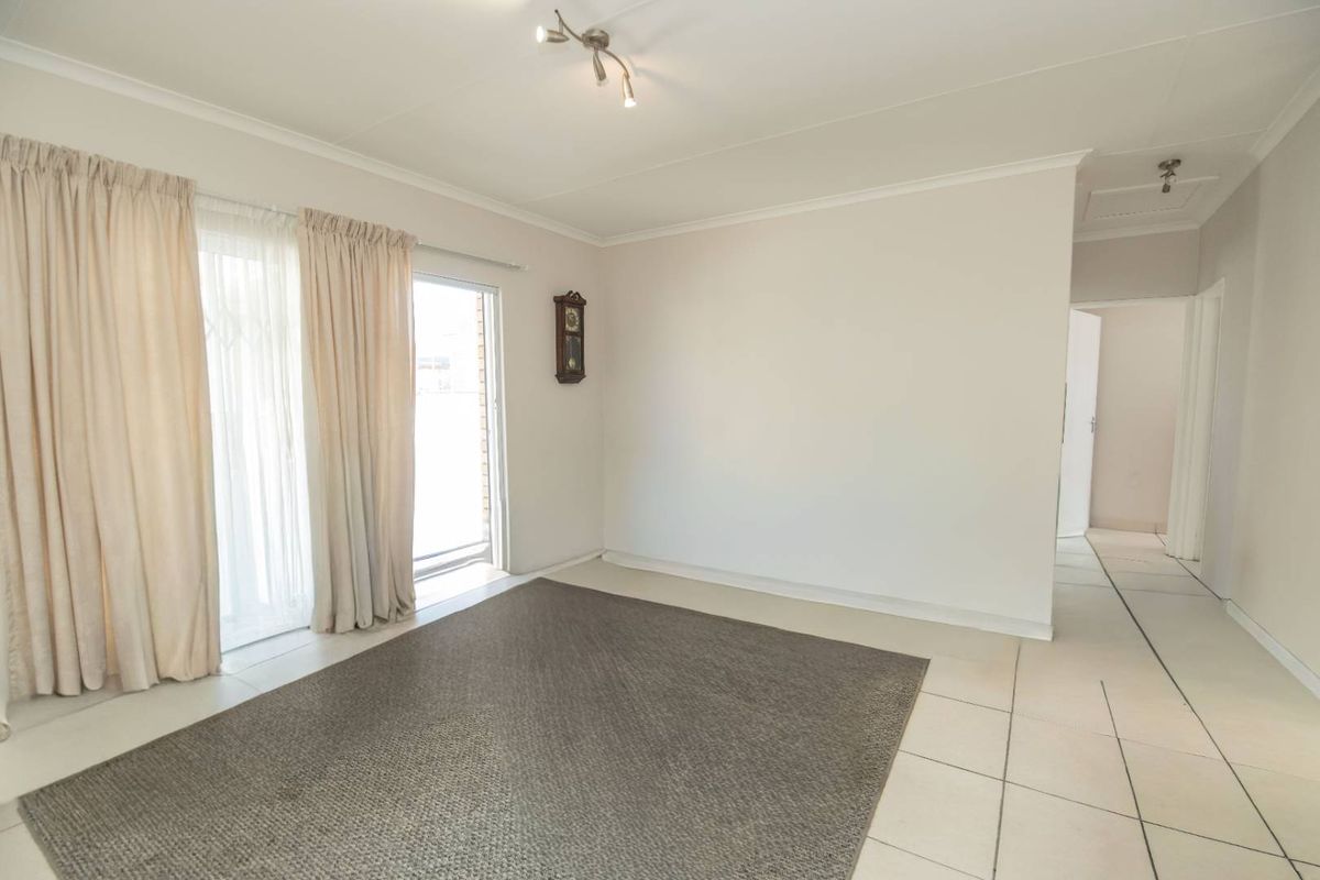 A bright and spacious living area featuring neutral tiled flooring, coved ceilings, and sliding glass doors providing access to the exterior.