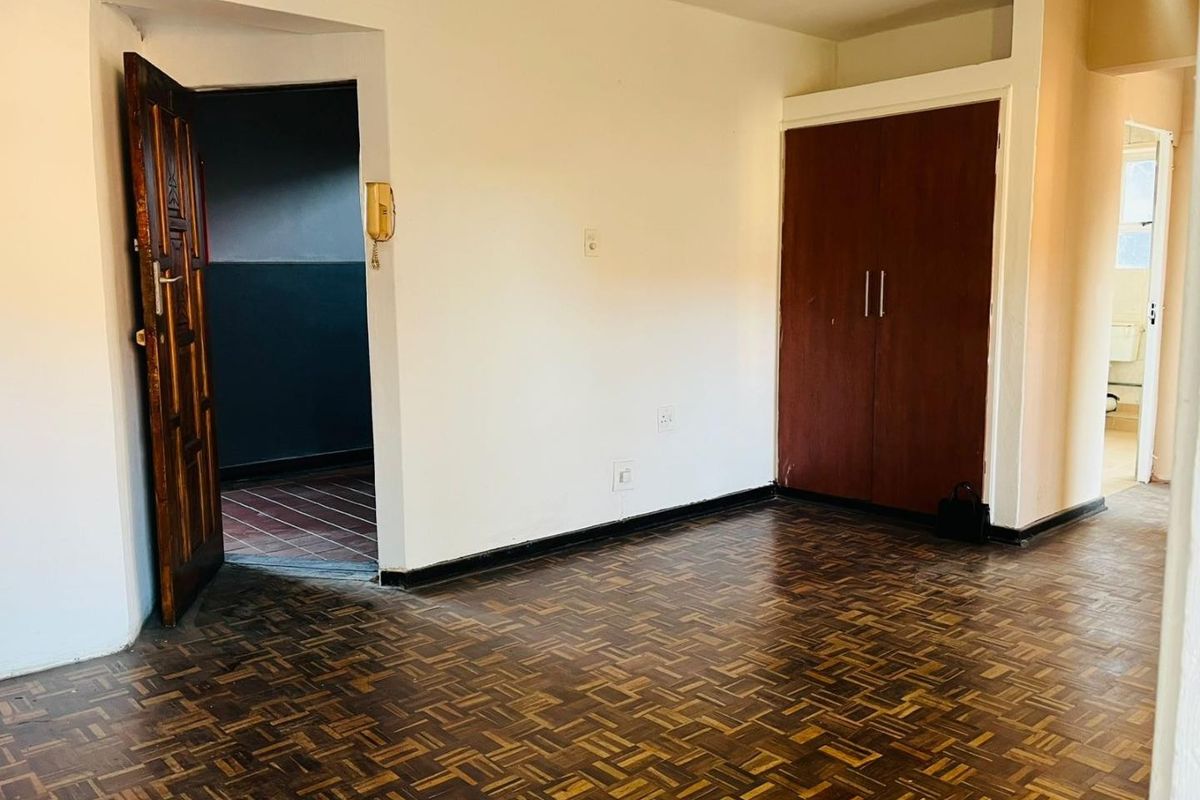 A vacant bedroom featuring traditional parquet flooring, a built-in wooden wardrobe, and an intercom system, offering a blank canvas for renovation.
