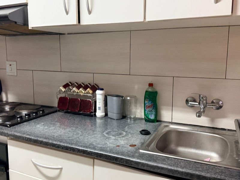 A functional kitchen area featuring white cabinetry, a dark laminate countertop, a stainless steel sink, and a built-in electric hob with an extractor fan.