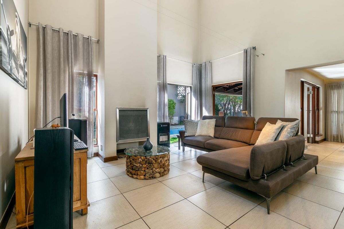 Spacious living room featuring double volume ceilings, tiled flooring, and a built-in fireplace with direct access to the outdoor pool area.