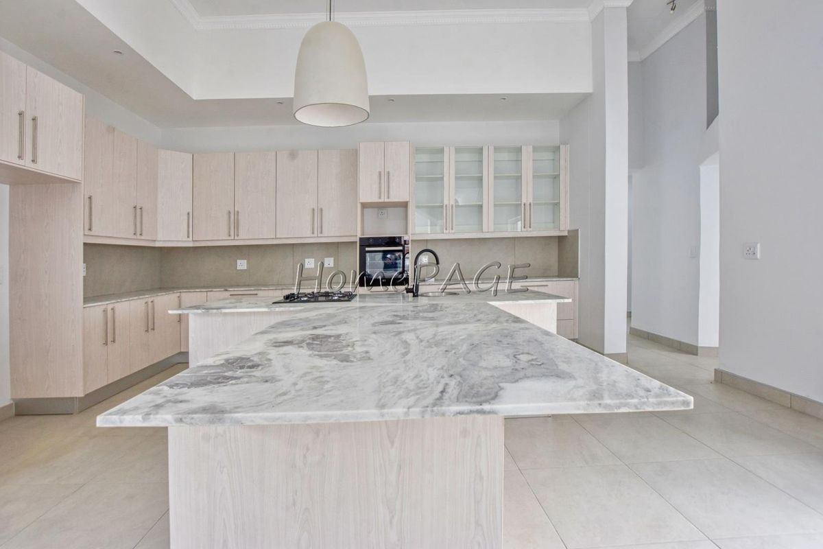 Modern kitchen featuring light wood cabinetry, a large marble-topped island, built-in oven, gas hob, and glass-fronted display cabinets.