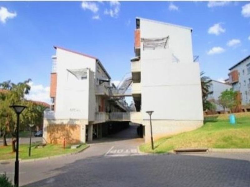Exterior view of a multi-story apartment complex featuring paved driveway access, connecting pedestrian bridges, and external staircases.