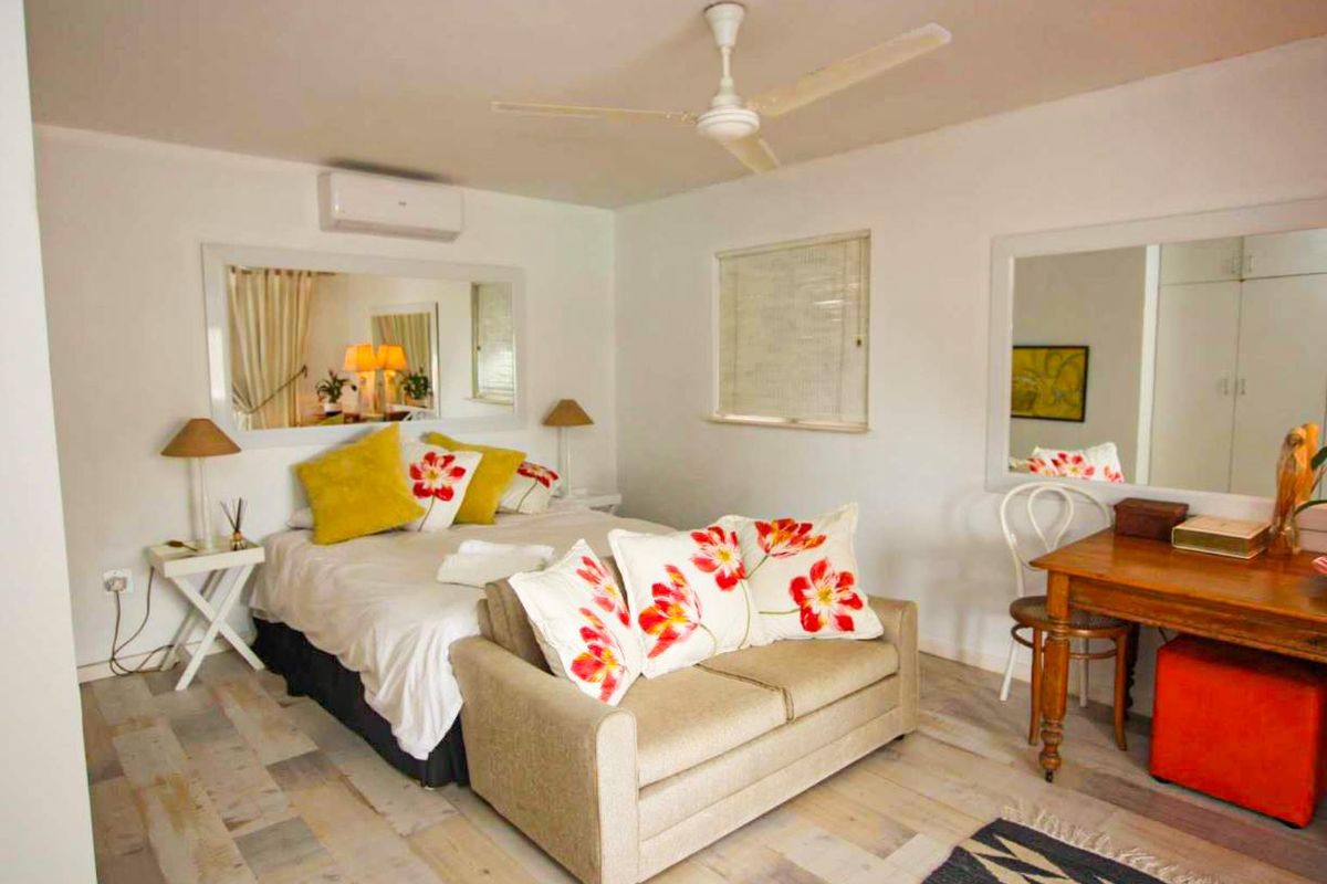 A well-lit bedroom featuring a ceiling fan, wall-mounted air conditioning unit, and built-in wardrobe storage.